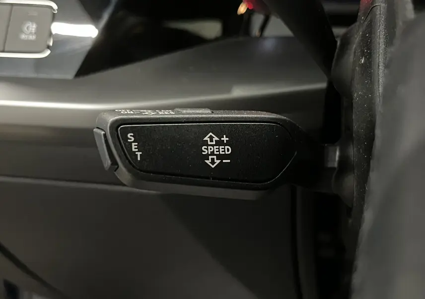 Gros plan sur la commande de régulateur de vitesse au volant d'une Audi A3 Sportback 30 TFSI bleu métallisé.