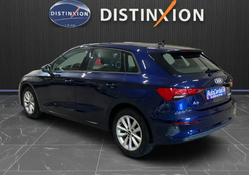 Audi A3 Sportback bleu métallisé vue 3/4 arrière droit, avec jantes argentées et vitres teintées, en intérieur showroom.