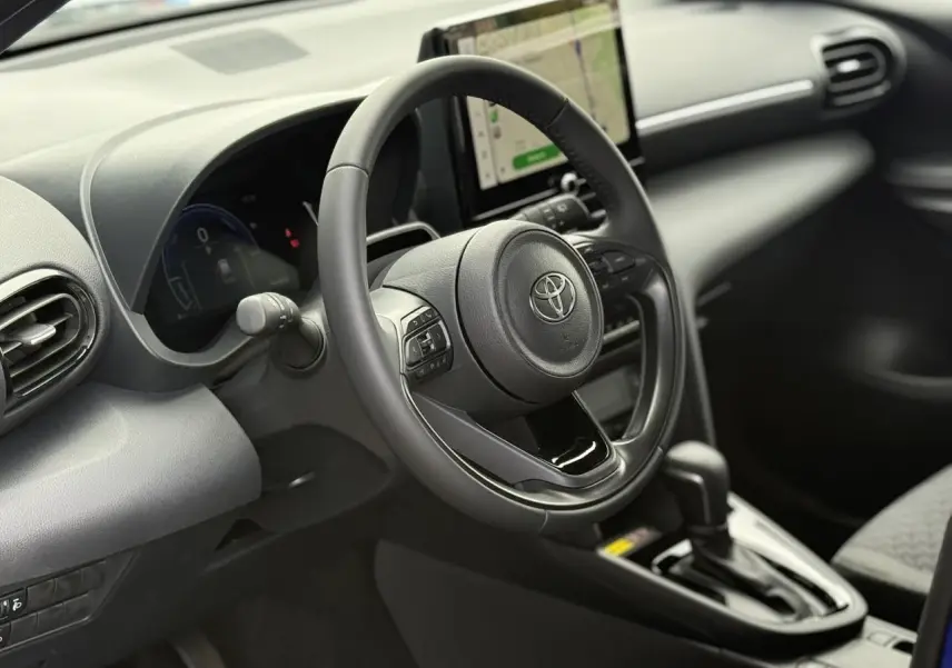 Vue intérieure côté conducteur du Toyota Yaris Cross 2026, volant cuir et écran tactile central visible.