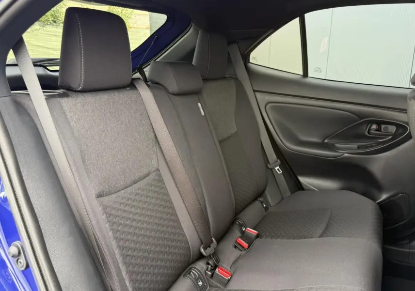 Vue latérale droite des sièges arrière noirs du Toyota Yaris Cross 1.5 Hybrid 116 Design bleu Genievre, avec ceinture de sécurité visible.