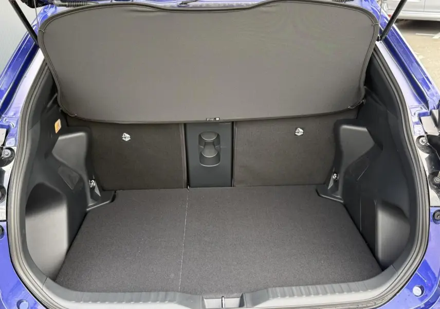 Coffre ouvert vu de l'arrière d'une Toyota Yaris Cross 1.5 Hybrid bleu Genievre avec plancher plat et cache-bagages.