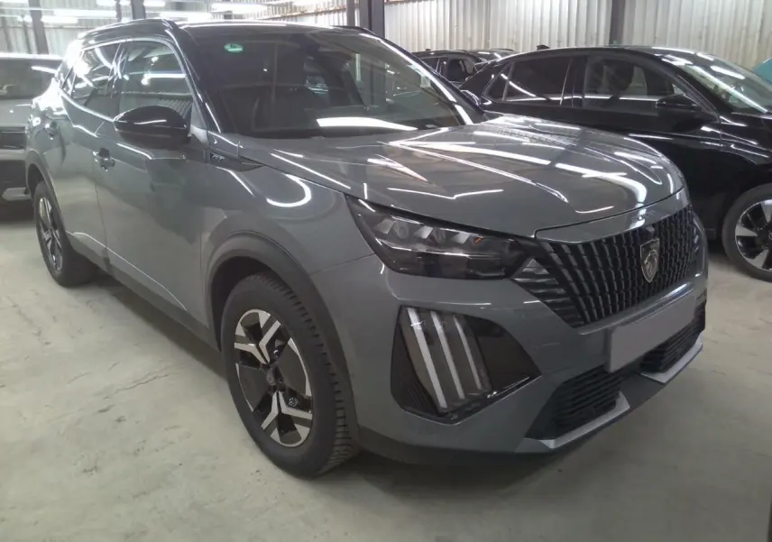 Peugeot 2008 1.2 Hybrid 145ch GT gris selenium en 3/4 avant avec barres de toit noires et calandre distinctive.