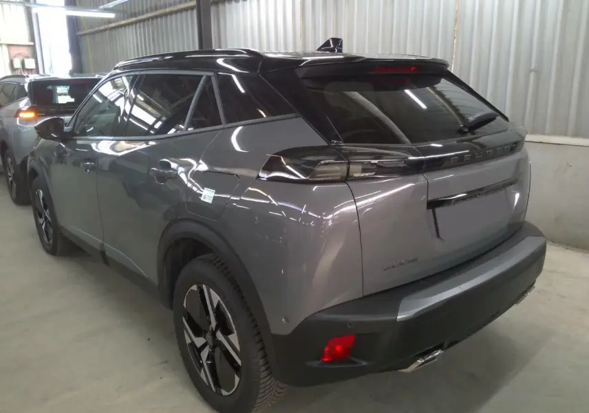 Peugeot 2008 gris selenium vue 3/4 arrière droit avec barres de toit noires dans un garage.