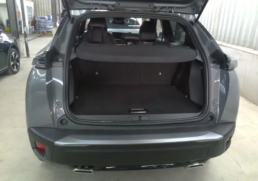 Vue arrière ouverte du coffre d'un Peugeot 2008 gris selenium, soulignant l'espace de chargement et les feux arrière.