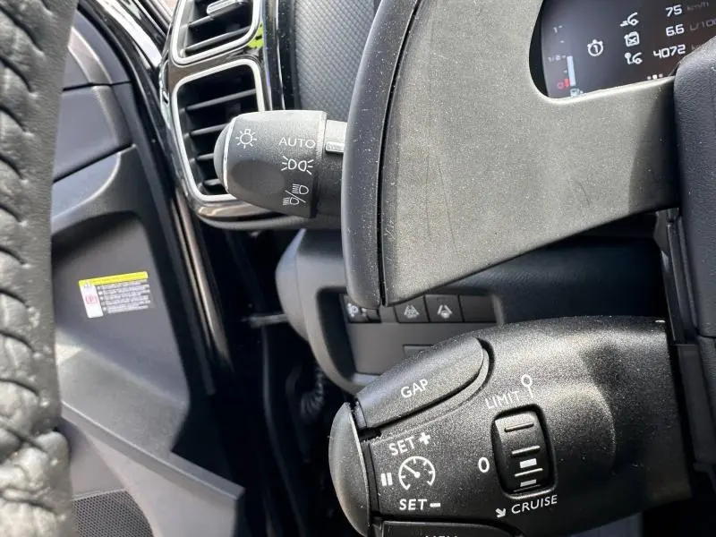 Gros plan sur les commandes au volant du Citroën C5 Aircross 2025 noir Perla Nera, mettant en valeur les fonctions régulateur et éclairage.
