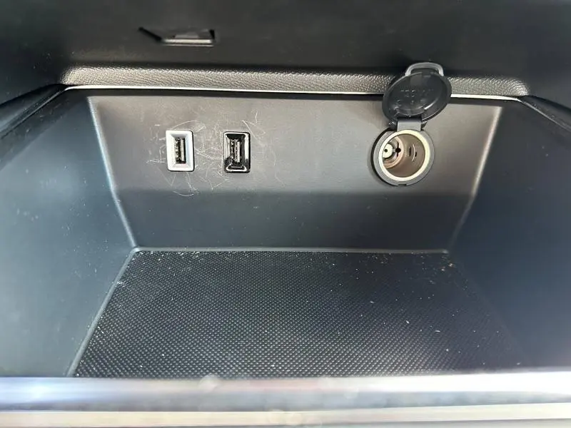 Gros plan sur la console centrale noire du Citroën C5 Aircross 2025 avec deux ports USB et une prise 12V ouverte.