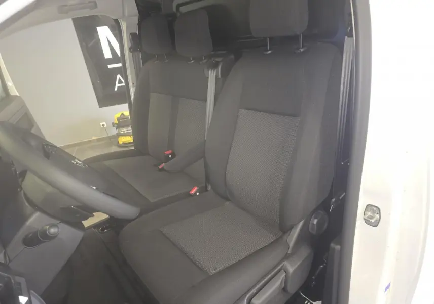 Vue intérieure côté conducteur de l'Opel Vivaro blanc, montrant la banquette et le siège avant en tissu noir.