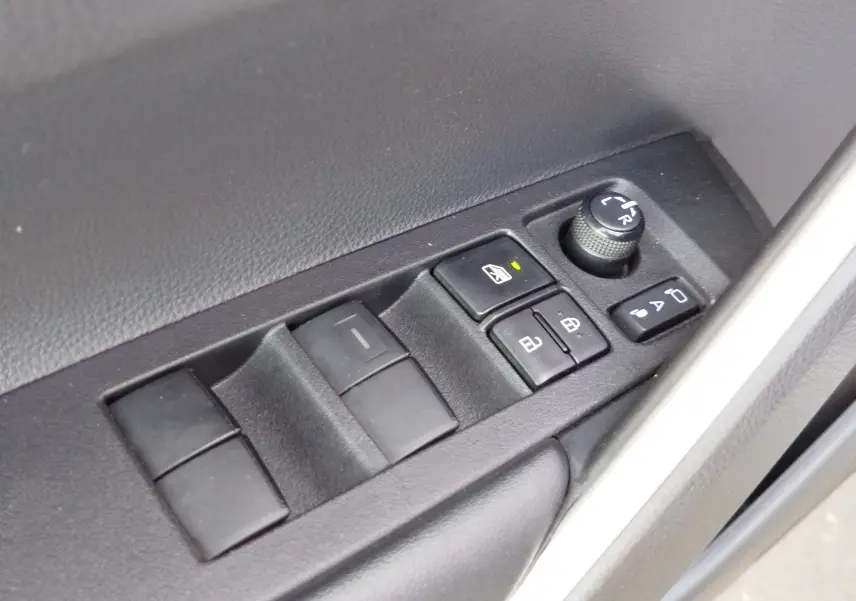 Gros plan sur les commandes de lève-vitres et réglage des rétroviseurs côté conducteur d'une Toyota Corolla Cross gris minéral.