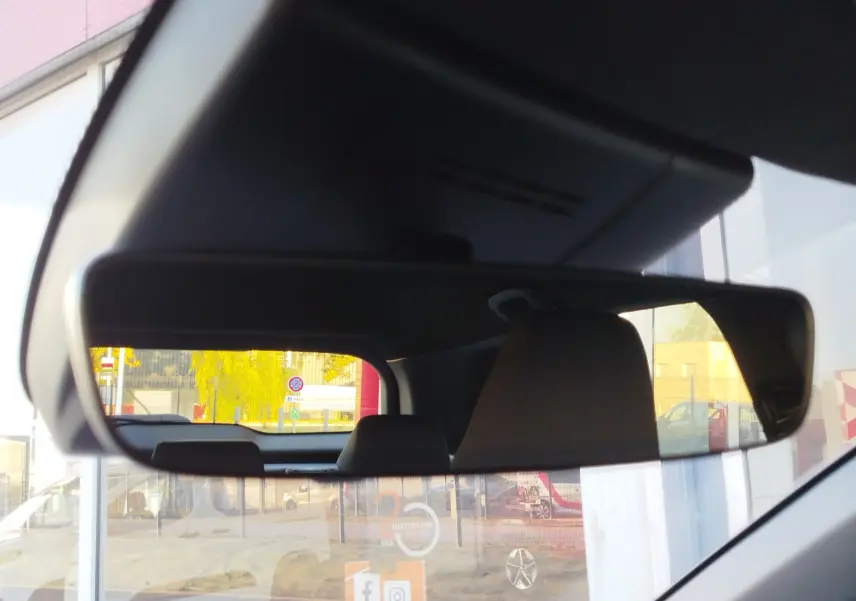 Vue intérieure du rétroviseur central d'une Toyota Corolla Cross gris minéral, reflétant l'arrière du véhicule et un environnement urbain.