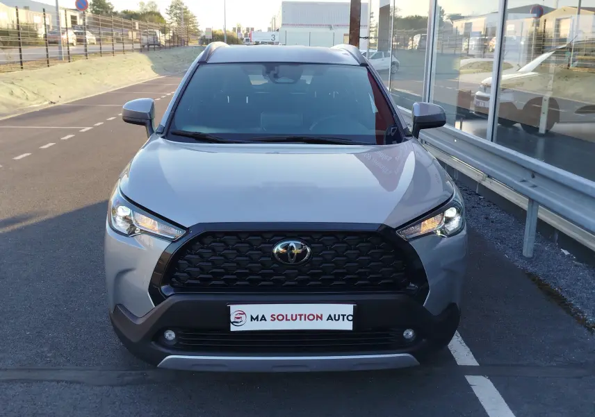 Vue avant centrée du Toyota Corolla Cross 2025 gris minéral avec calandre noire et feux LED allumés.