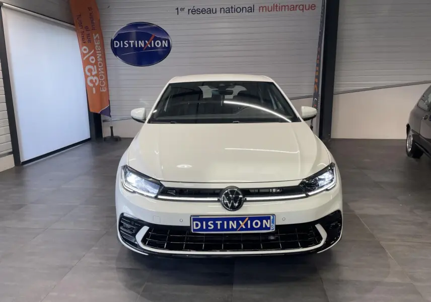 Vue avant d'une Volkswagen Polo blanche 2024 R-Line avec calandre spécifique et feux LED allumés en showroom.
