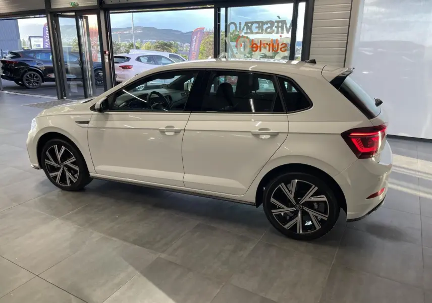 Volkswagen Polo 1.0 TSI R-Line blanche vue de profil côté gauche en intérieur avec jantes alliage noires et chromées.