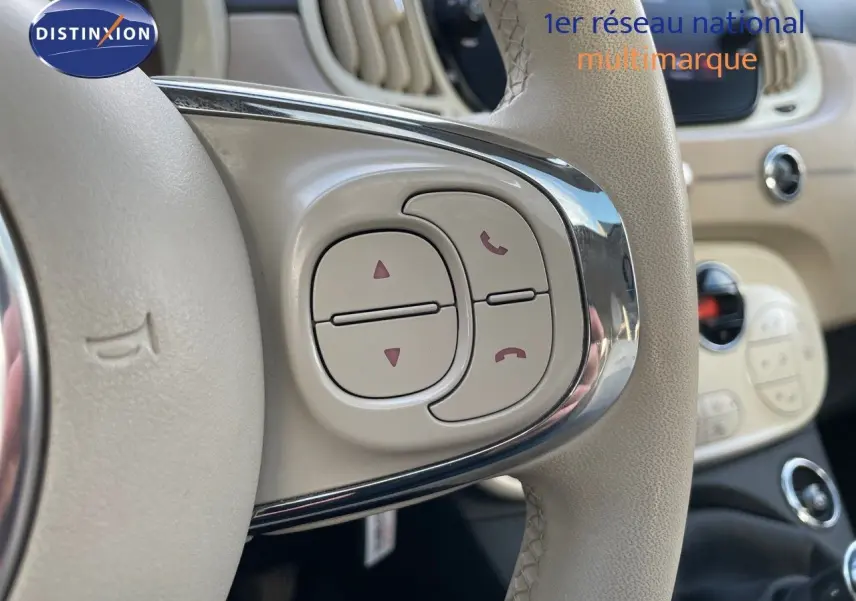 Gros plan sur les commandes du volant beige de la FIAT 500 blanche, mettant en valeur les boutons de gestion d'appels et navigation.