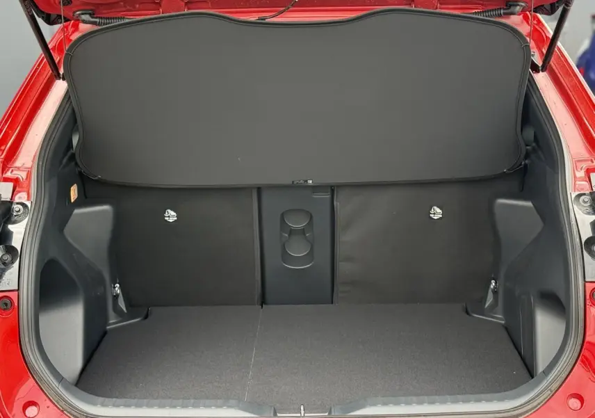 Coffre ouvert vu de l'arrière d'une Toyota Yaris Cross rouge intense, montrant un plancher plat et un cache-bagages noir.