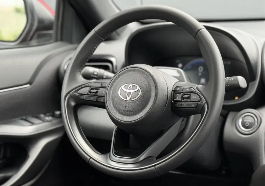 Gros plan sur le volant cuir noir de la Toyota Yaris Cross 2026, avec commandes intégrées et tableau de bord flou en arrière-plan.