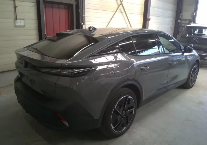 Vue 3/4 arrière droite d'une Peugeot 408 HYBRID 145 GT gris selenium, avec toit noir et jantes distinctives en alliage.