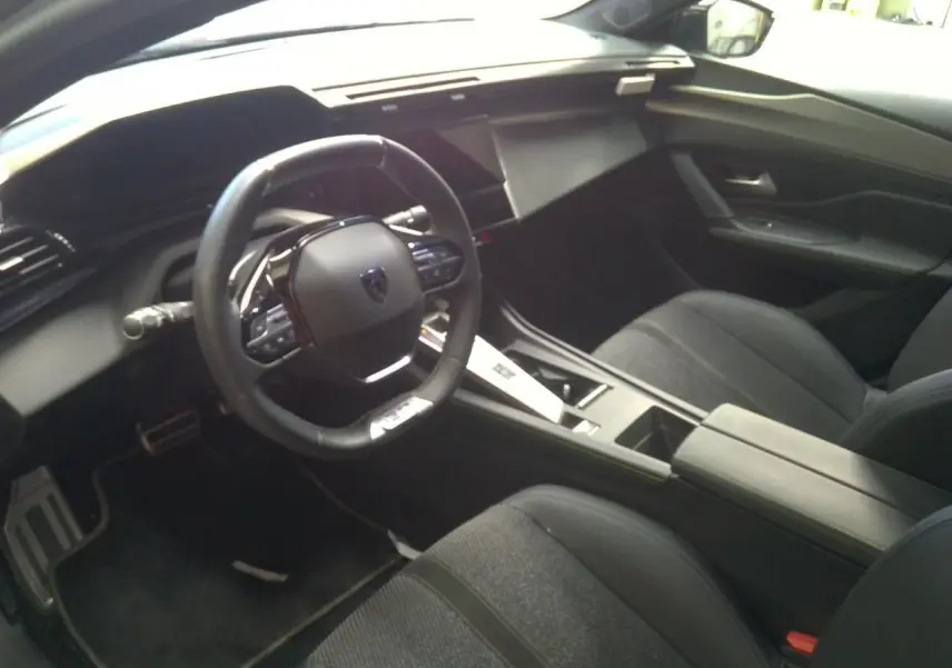 Vue intérieure côté conducteur de la Peugeot 408 Hybrid 145 GT 2025, tableau de bord et volant noirs modernes.