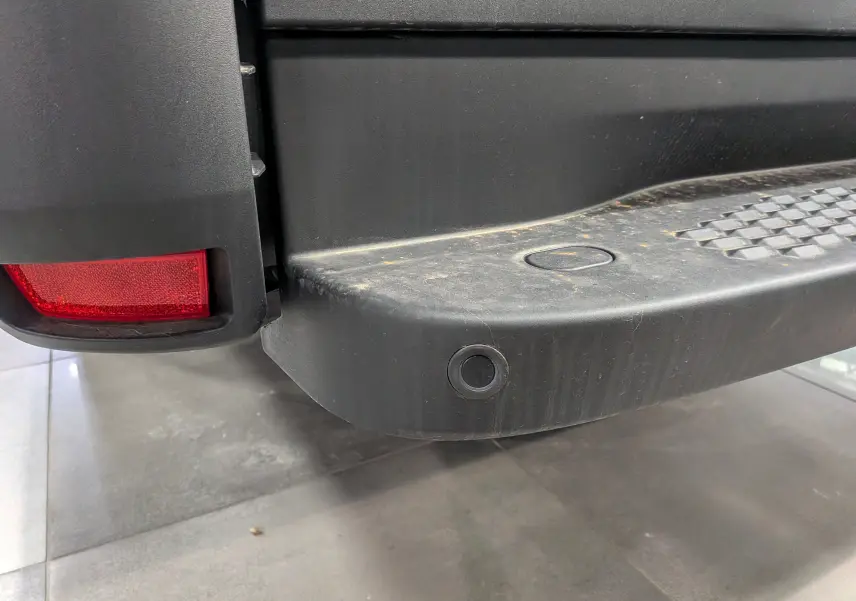 Gros plan sur le pare-chocs arrière noir avec capteur de recul et feu rouge du fourgon Iveco Daily blanc.