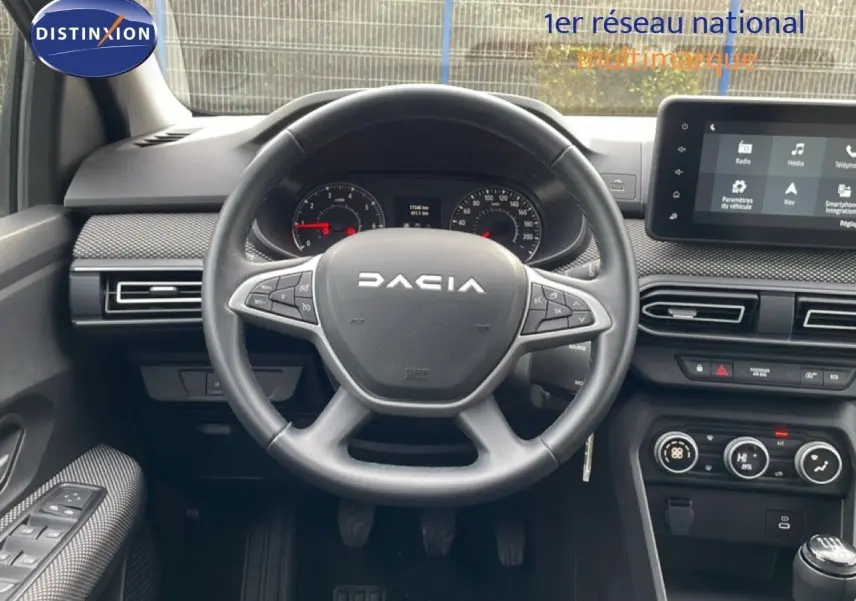 Vue intérieure centrée sur le volant DACIA noir et le tableau de bord avec écran tactile et commandes climatisation.