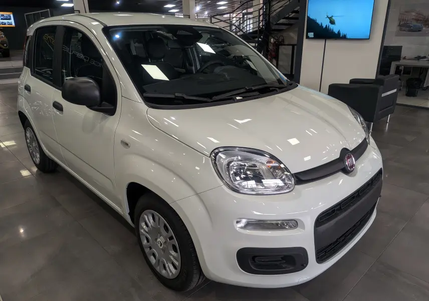 Vue 3/4 avant droite de la FIAT Panda 1.0 70 CH Hybrid City blanche Gelato en showroom, avec rétroviseurs noirs.