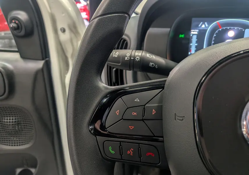 Gros plan sur le volant multifonction noir de la Fiat Panda 1.0 Hybrid 2025, avec porte ouverte côté gauche blanc Gelato.