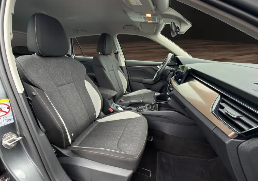 Vue intérieure côté gauche du Skoda Kamiq 2023 gris foncé, sièges tissu bicolore et tableau de bord bois clair.