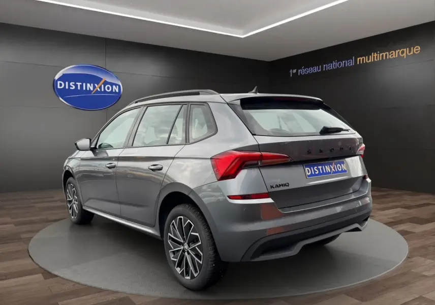 Vue 3/4 arrière droite d'un Skoda Kamiq gris foncé avec jantes bi-ton et caméra de recul en showroom.