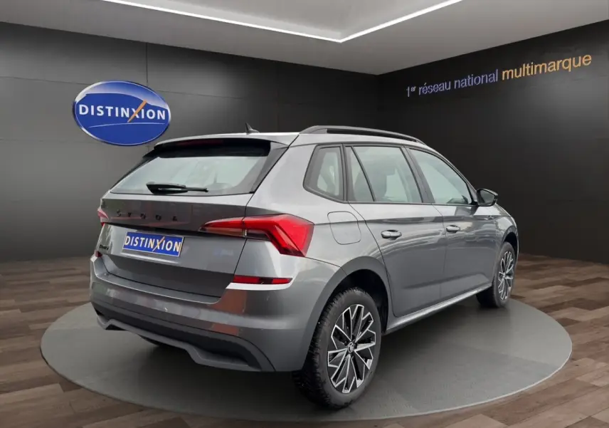 Vue 3/4 arrière droite d'un Skoda Kamiq gris foncé avec jantes bi-ton et caméra de recul en showroom.