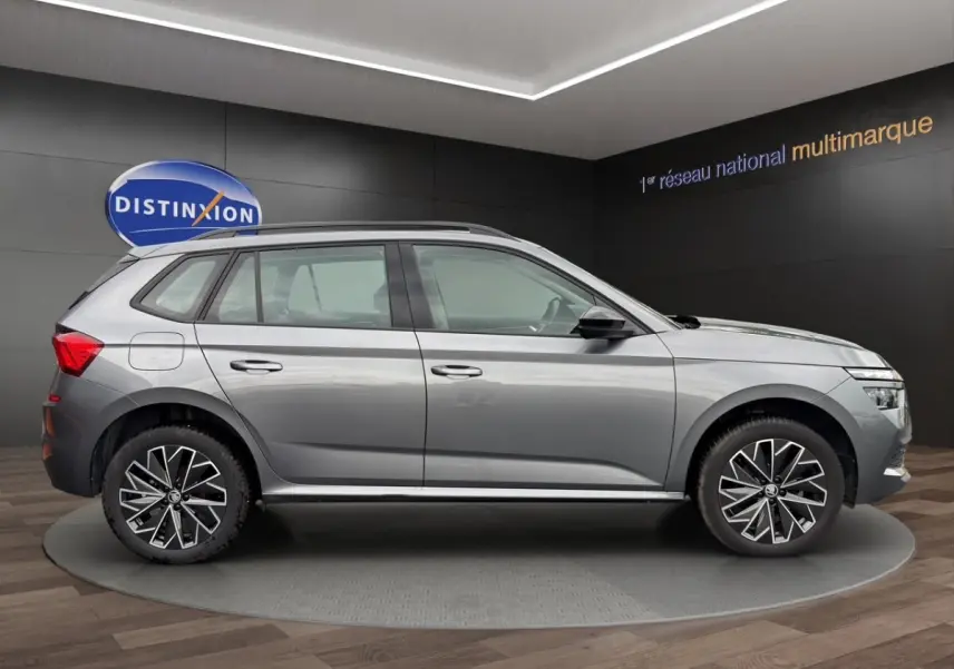 Vue de profil côté gauche d'un Skoda Kamiq gris foncé 2023 avec jantes bi-ton et barres de toit noires.