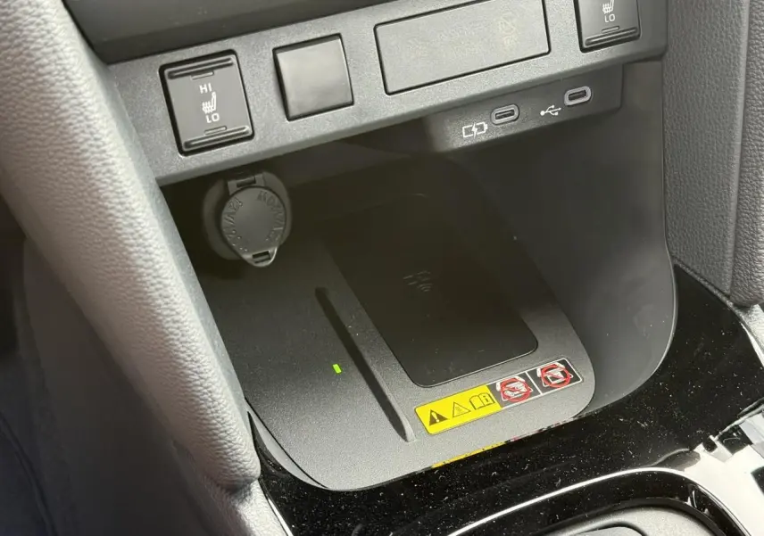 Gros plan sur la console centrale de la Toyota Yaris Cross 1.5 Hybrid 116 Design, montrant le chargeur à induction et commandes sièges chauffants.