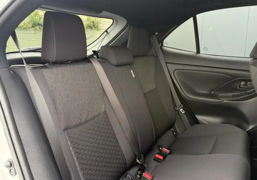 Vue intérieure des sièges arrière noirs du Toyota Yaris Cross 1.5 Hybrid 116 Design avec ceinture de sécurité et porte latéral visible.