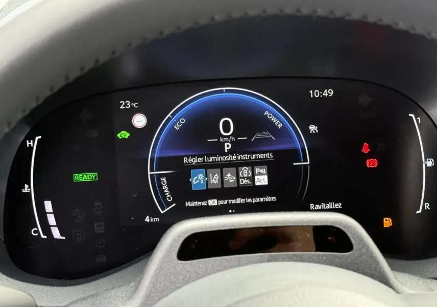 Vue rapprochée du tableau de bord numérique de la Toyota Yaris Cross blanc lunaire, affichant les instruments et alertes.