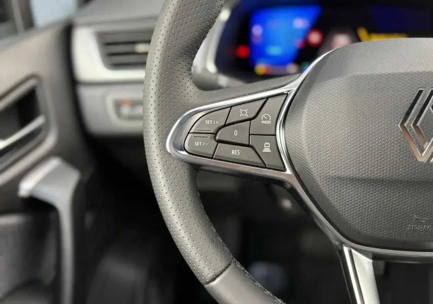 Gros plan sur le volant en cuir perforé avec commandes multifonctions du Renault SYMBIOZ noir étoile, tableau de bord flou en arrière-plan.