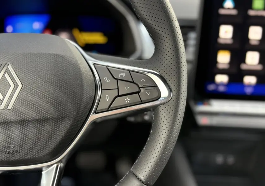 Gros plan sur le volant en cuir perforé de la Renault Symbioz 2025 avec commandes multifonctions et écran tactile flou en arrière-plan