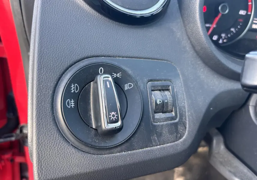 Gros plan sur le bouton de commande des phares à gauche du tableau de bord d'une SEAT Ibiza rouge clair de 2016.