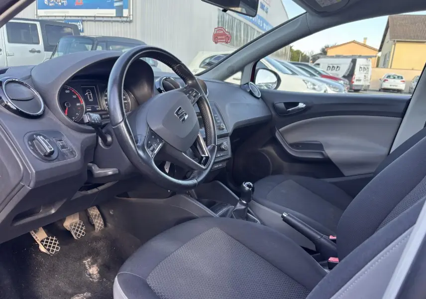Vue intérieure côté conducteur de la SEAT Ibiza 1.2 TSI 2016 avec volant cuir, boîte manuelle et sièges tissu gris.