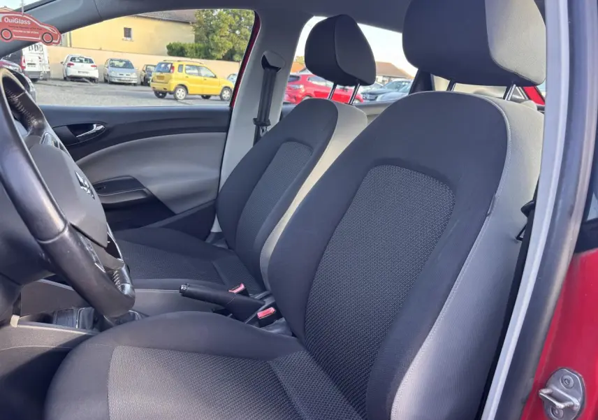 Vue intérieure côté conducteur de la SEAT Ibiza rouge clair 2016, montrant les sièges avant noirs et la portière ouverte.