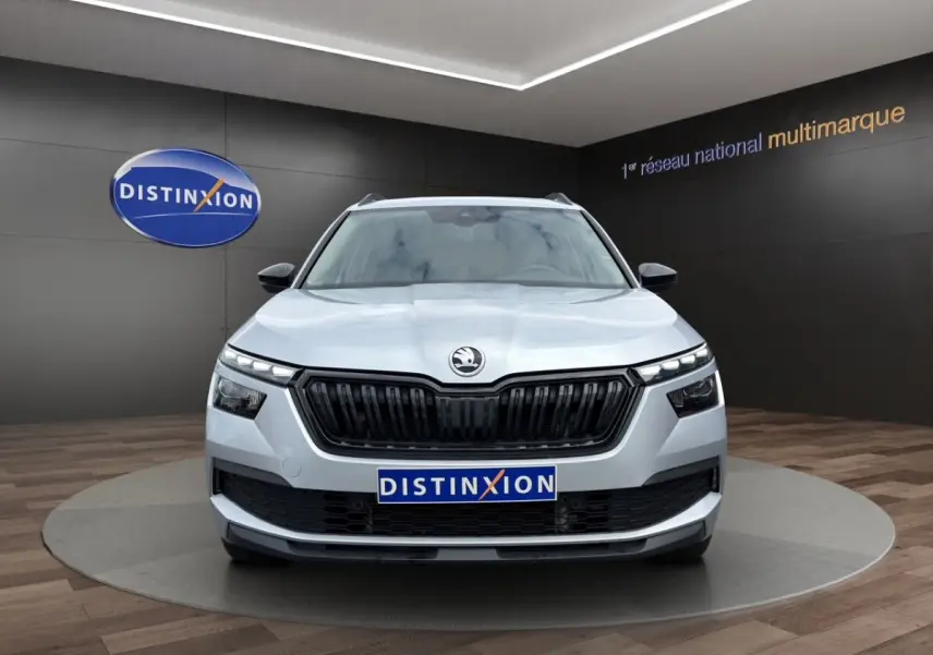 Vue 3/4 avant droite d'un Skoda Kamiq gris clair avec jantes bi-ton et rétroviseurs noirs dans un showroom.