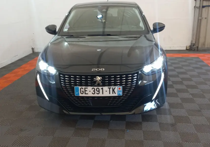 Peugeot 208 noire vue de face, phares LED allumés et signature lumineuse en forme de griffes visibles.