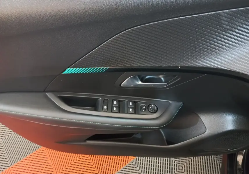 Vue intérieure côté gauche de la porte d’une Peugeot 208 noire, avec commandes des vitres et poignée intégrée.