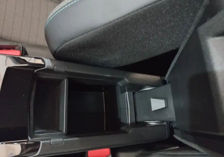 Vue rapprochée de la console centrale noire ouverte de la Peugeot 208 PureTech 100 Allure Pack, montrant le rangement intérieur.
