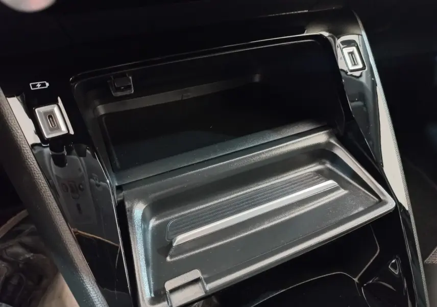 Gros plan intérieur sur la console centrale noire brillante avec compartiment ouvert et ports USB visibles.
