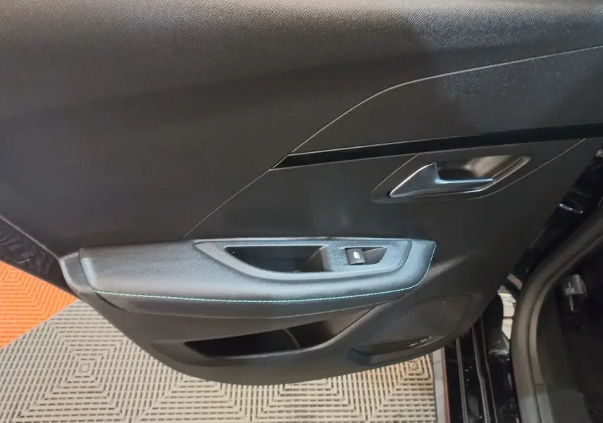 Gros plan sur la porte intérieure côté gauche noire de la Peugeot 208 PureTech 100 Allure Pack avec surpiqûres bleues.