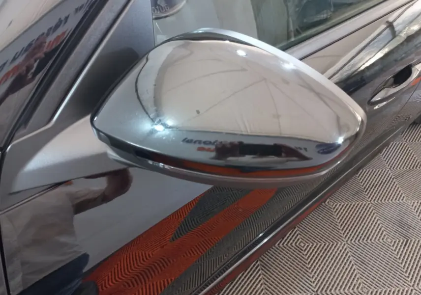 Rétroviseur chromé côté droit d'une Peugeot 208 noire, vue rapprochée avec reflet de l'environnement intérieur.
