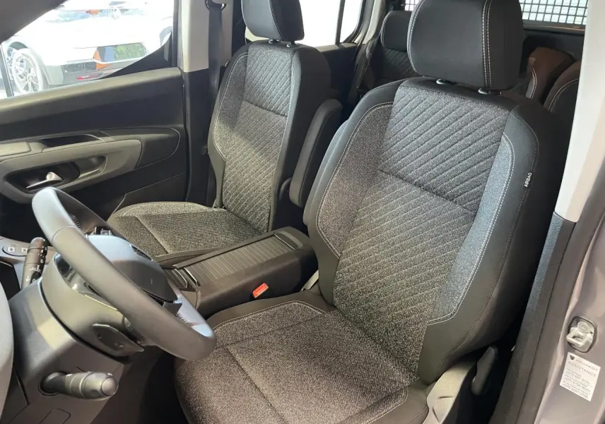 Vue intérieure sur les sièges avant en tissu gris du Peugeot Rifter 2026, avec volant cuir multifonction visible côté gauche.