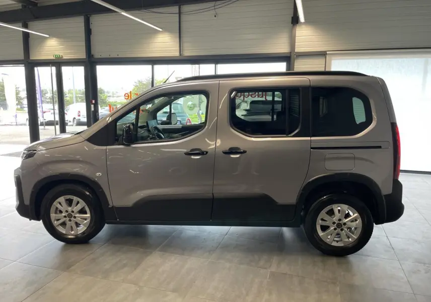Profil côté gauche du Peugeot Rifter gris Artense 2026 avec portes coulissantes et jantes tôles 16 pouces en showroom.