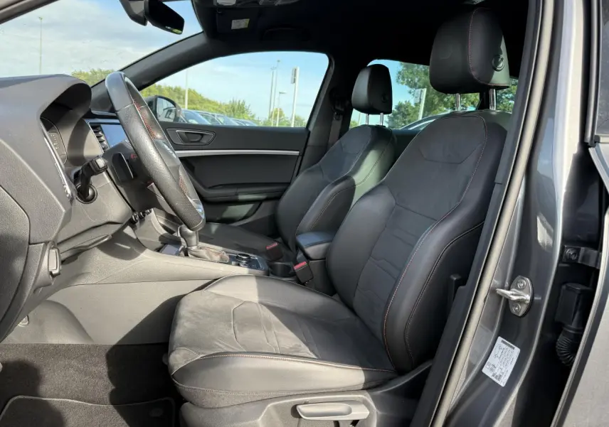 Intérieur côté conducteur du SEAT Ateca gris graphite 2023, sièges sport noirs avec surpiqûres rouges et volant cuir.