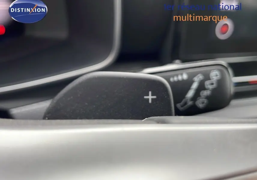 Gros plan sur la palette de changement de vitesse "+" du volant d'une SEAT LEON ST 2023 gris urbain, intérieur moderne.