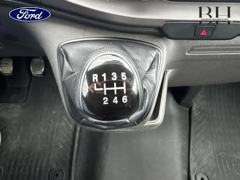 Le levier de vitesses manuel noir du Ford Transit Custom Fourgon 2023 vu de dessus, avec console et pédales visibles.