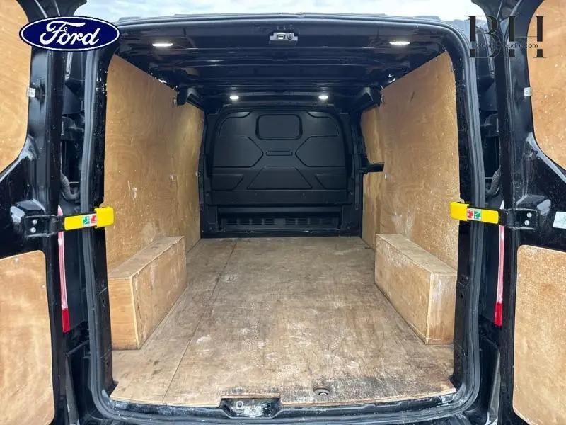 Vue arrière intérieure du Ford Transit Custom noir Agate, montrant l'espace de chargement en bois clair et l'éclairage LED plafond.